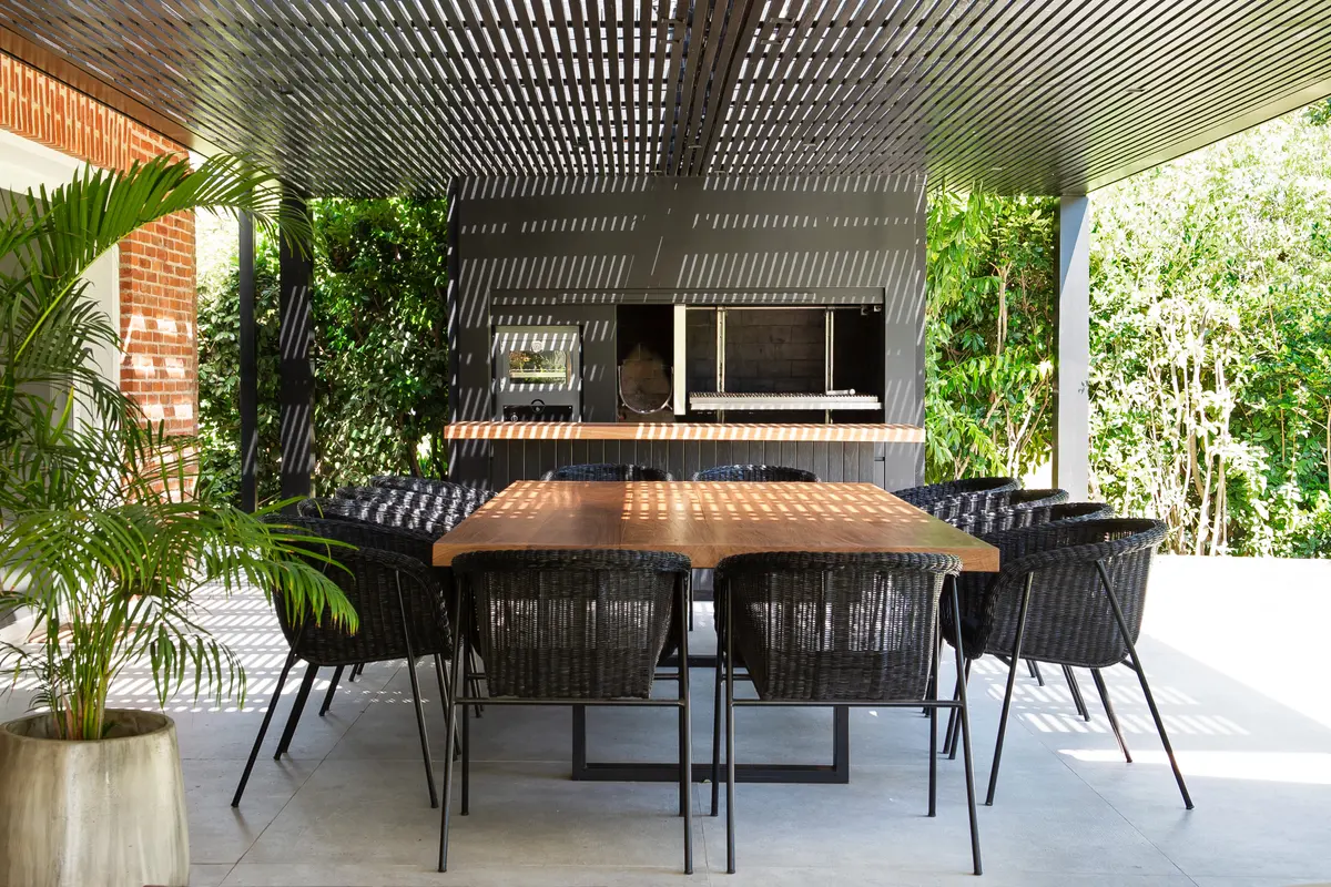 Comedor exterior y área de asado bajo pérgola moderna — proyecto Quincho SA, por Estudio Junor, en Pilar